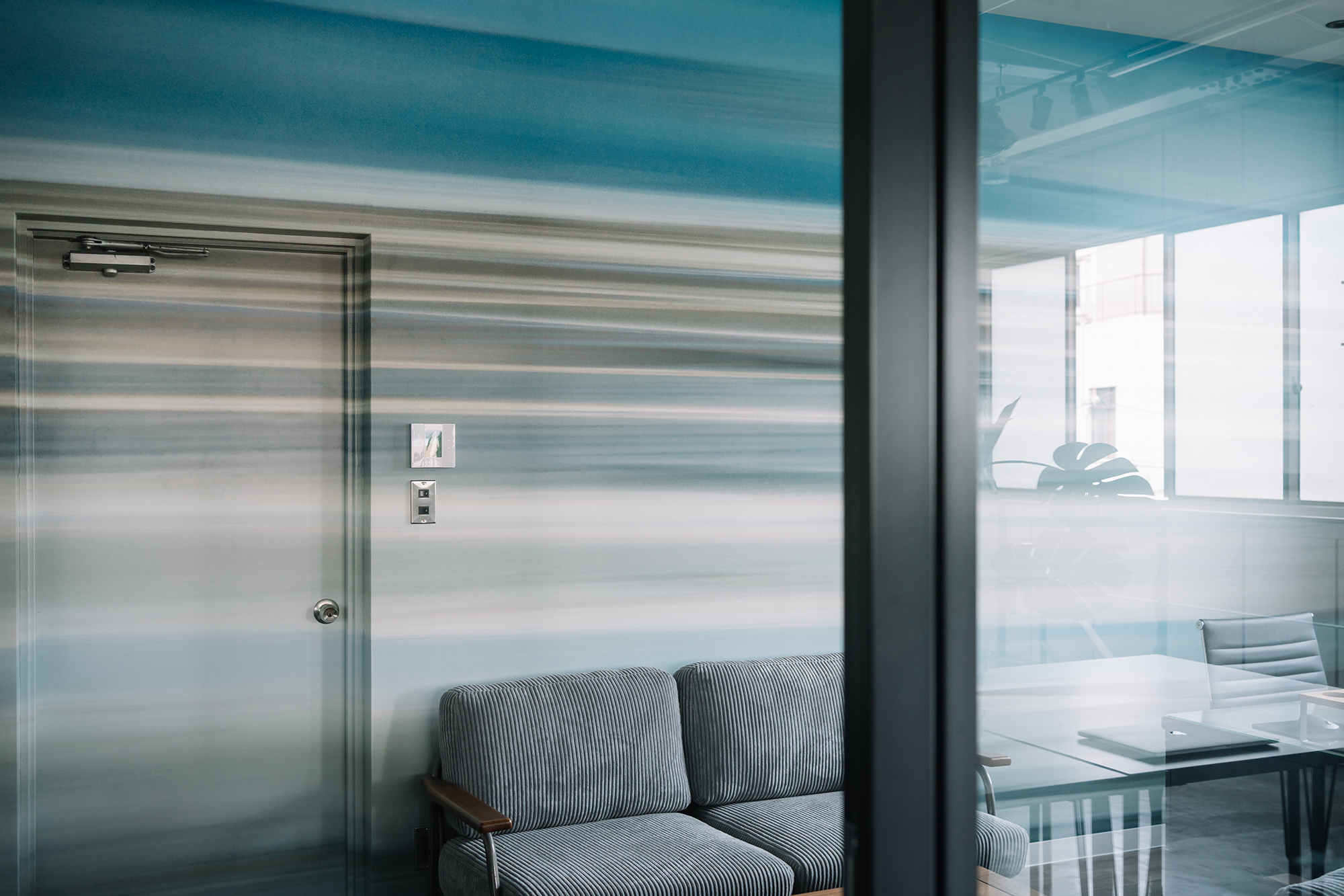 大阪府大阪市のオフィス壁面とドアを、さまざまなブルーの横のラインがグラデーションのように流れるデザインで仕上げた
